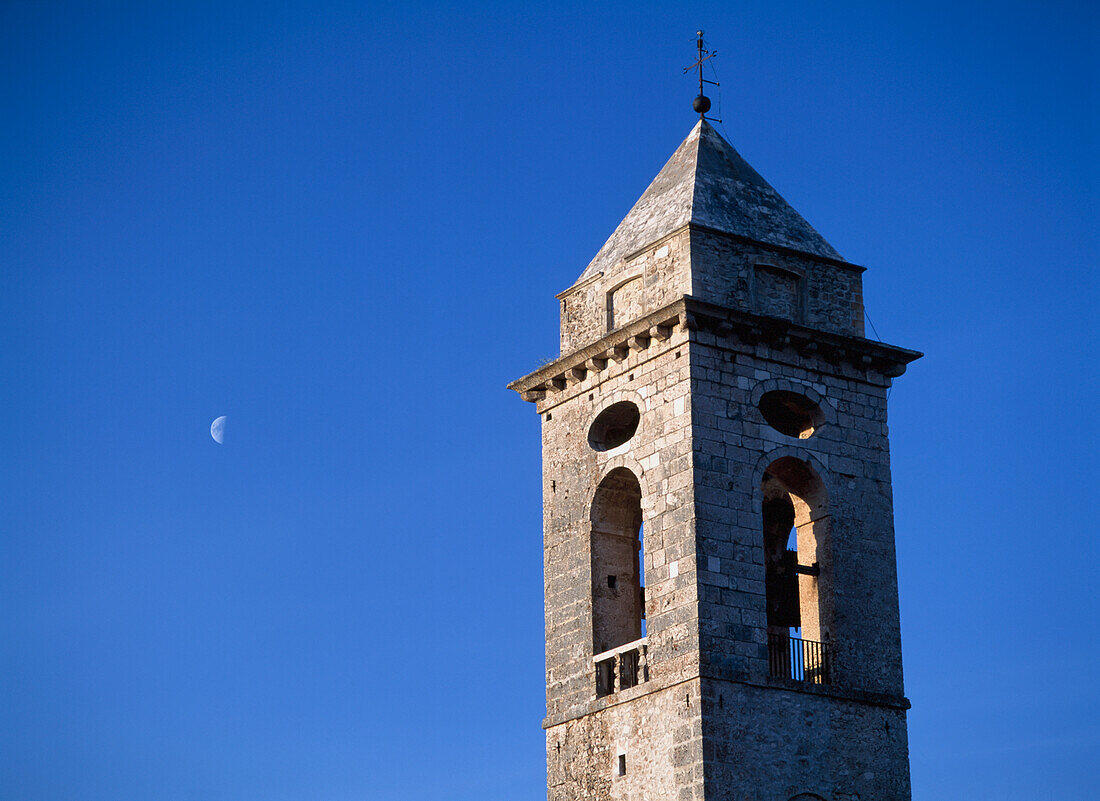 Der Glockenturm der Kirche Santo Stefano Di Sessanio mit dem Mond dahinter in der Abenddämmerung, Abruzzen, Italien.