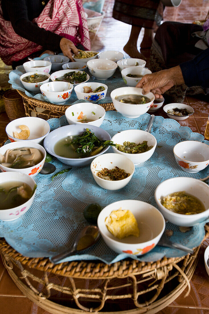 Junge Reisende genießt das Frühstück mit älteren einheimischen Frauen im Tempel, Schalen auf Tischen in Vang Vieng, Laos