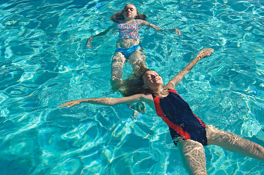 Zwei Mädchen (12-13) schwimmen auf dem Wasser im Schwimmbad