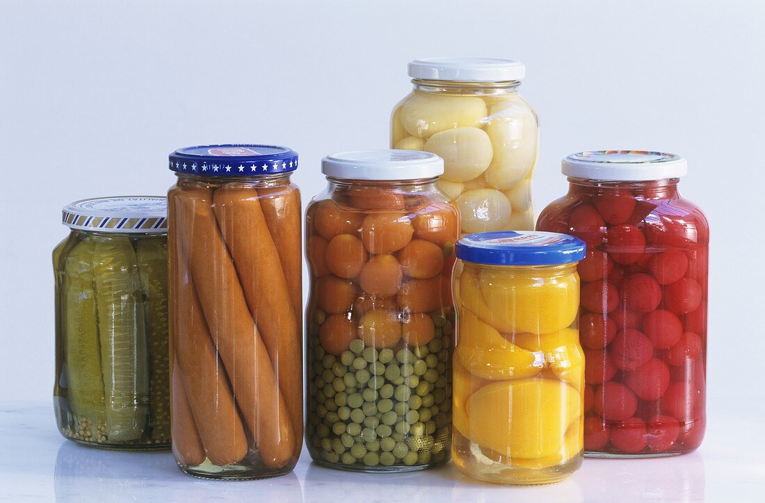 Six preserving jars with vegetables, fruit, sausages