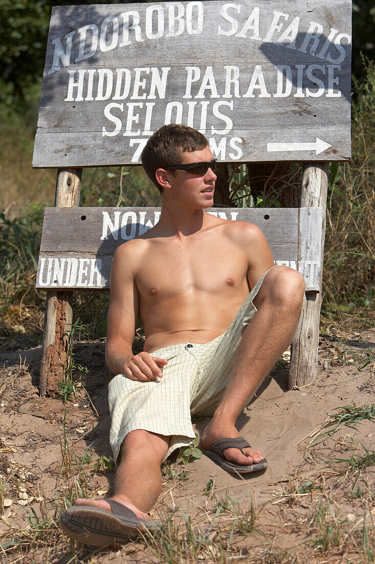 Man Sitting By Safari Camps Signs In Selous National Park, Tanzania,East Africa