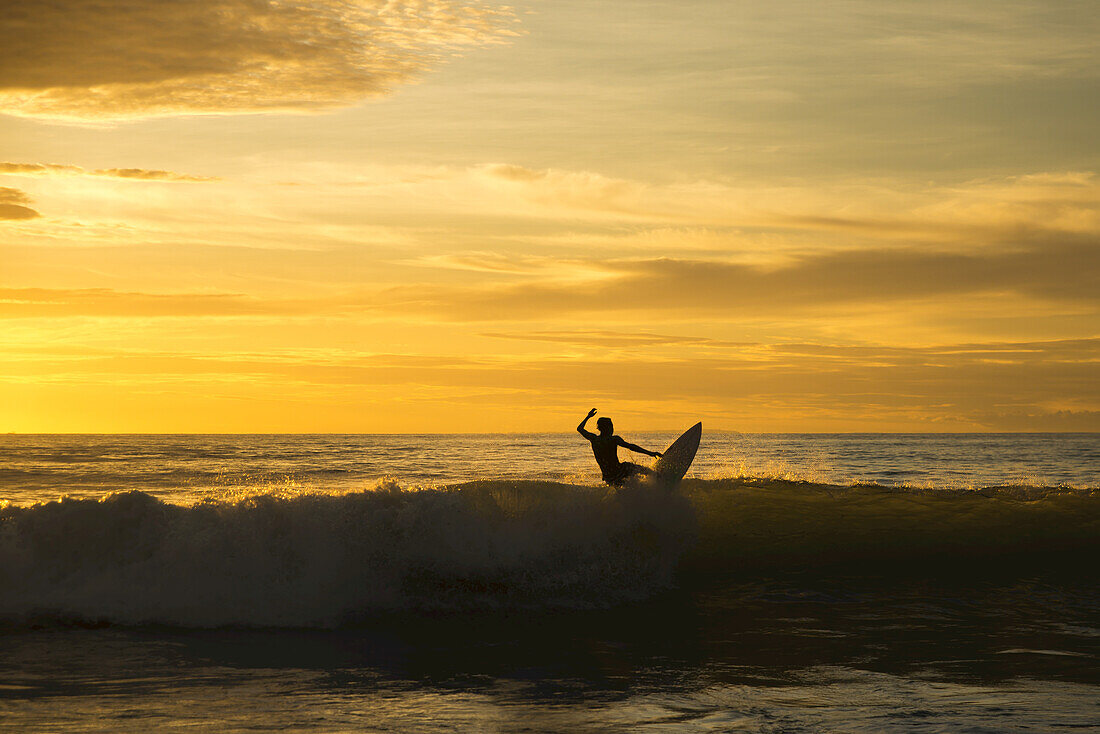 Surfer reitet eine Welle bei Sonnenuntergang, Dreamland Beach; Insel Bali, Indonesien