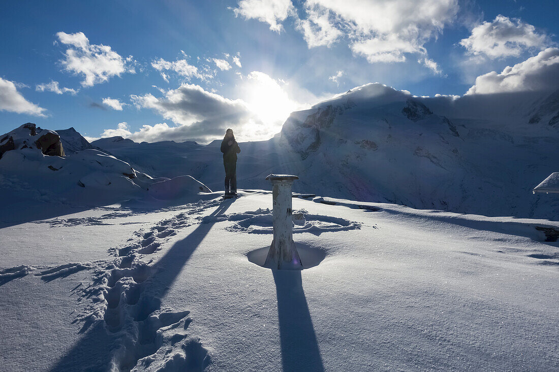 Eine Frau steht bei Sonnenaufgang im Schnee auf dem Gornergrat-Gipfel, Monte Rosa, Penninische Alpen; Zermatt, Wallis, Schweiz