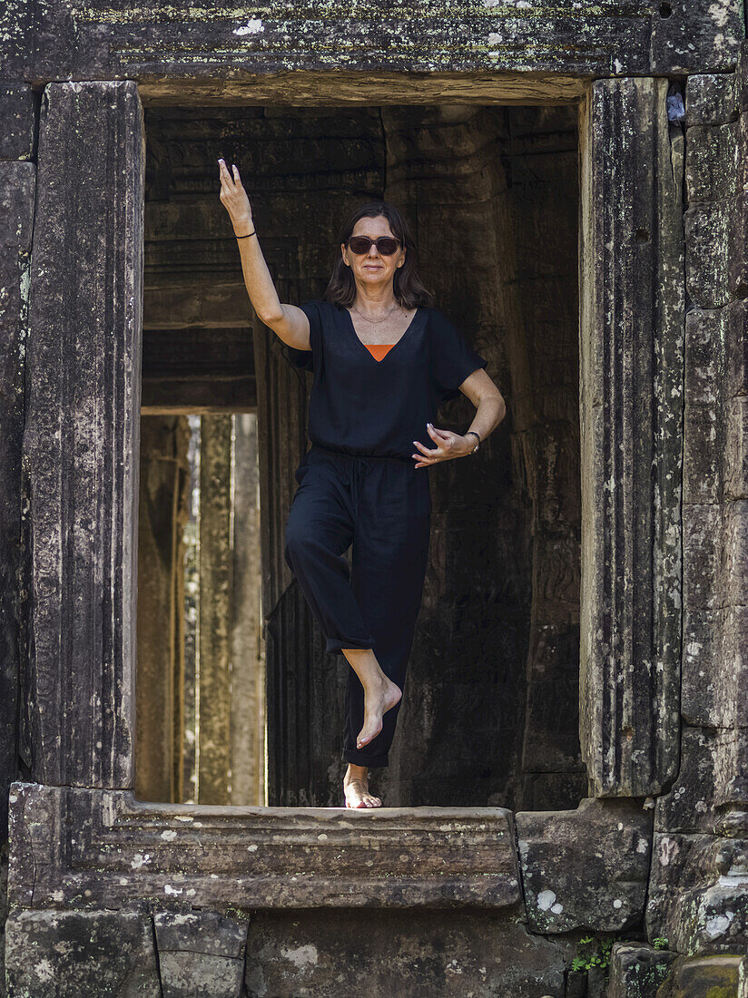 Eine Frau steht in einer Yoga-Pose in einer Öffnung des Bayon-Tempels, Angkor Thom; Krong Siem Reap, Provinz Siem Reap, Kambodscha.