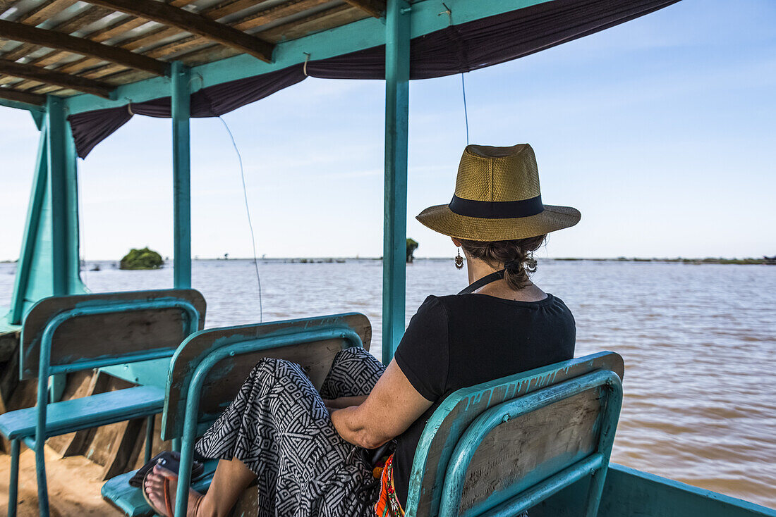 Eine Frau sitzt auf einem Boot und schaut auf das Wasser, während es einen Fluss hinunterfährt; Provinz Siem Reap, Kambodscha
