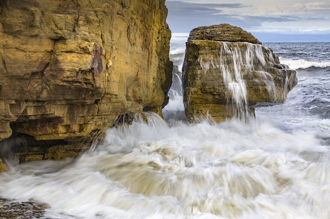 Die einlaufende Flut plätschert an einem Felsen an der nordostenglischen Küste; Whitburn, Tyne and Wear, England.