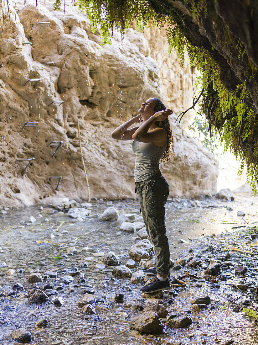 A Young Woman Stands On A Rock And Looks Up Along A Stream At Dodim Cave, Ein Gedi Nature Reserve; South District, Israel