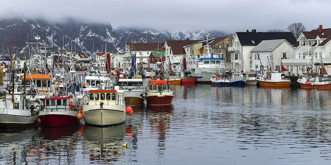 Boote im Hafen und Gebäude am Ufer bei tief hängenden Wolken; Lofoteninseln, Nordland, Norwegen