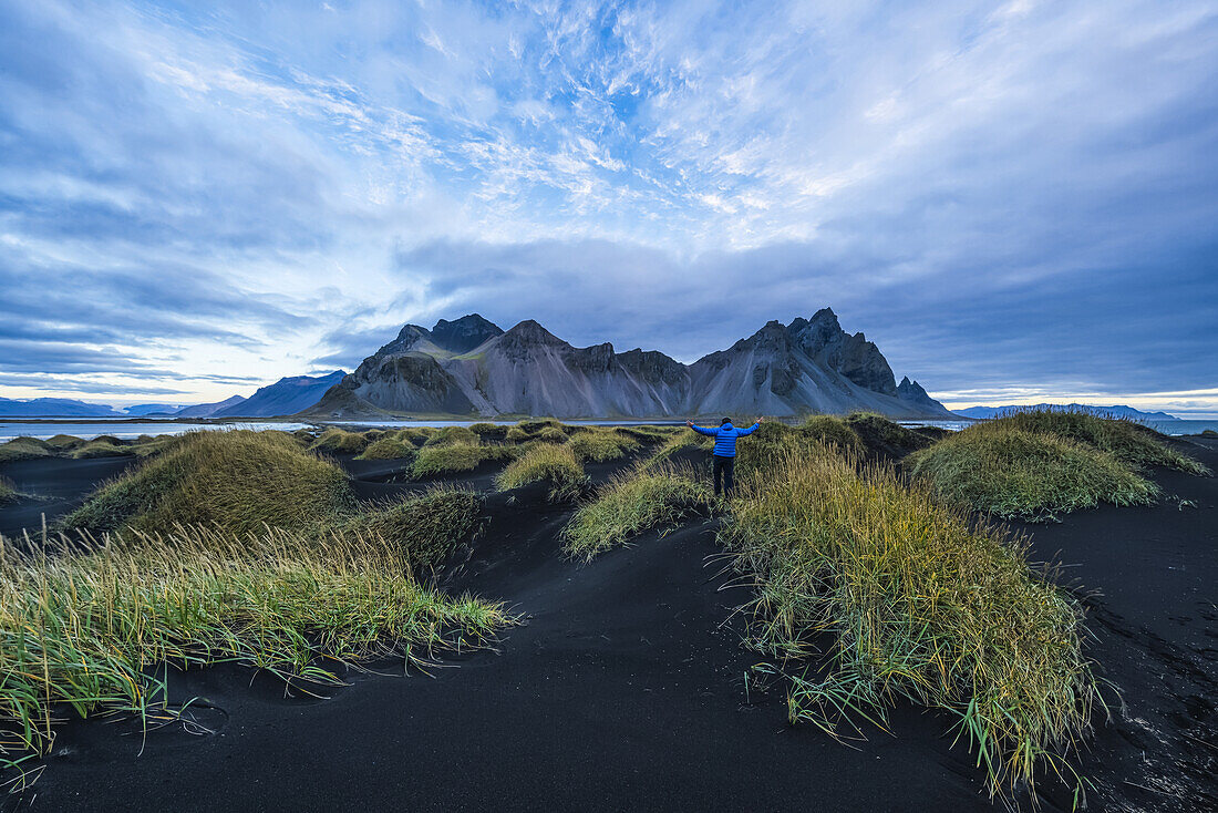 Person Standing On A Black Sand Mound Looking At Vestrahorn Or Stokknes On The South Coast Of Iceland; Hofn, Iceland
