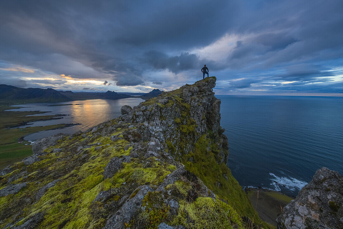 Eine Person steht und betrachtet die Aussicht von der Spitze einer Meeresklippe entlang der Strandir-Küste; Westfjorde, Island
