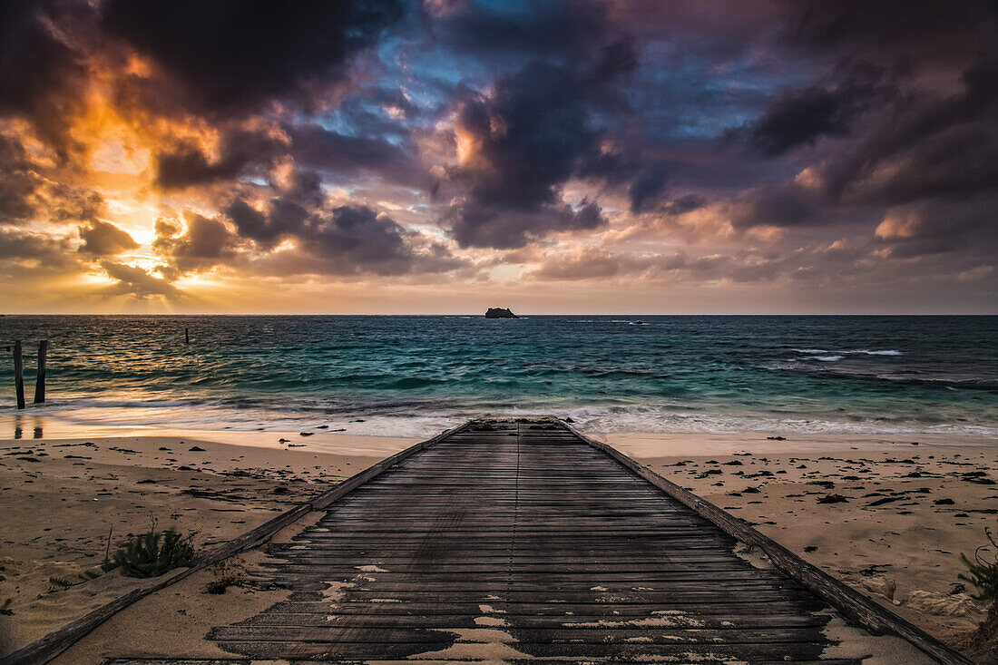 A wooden boardwalk on a beach leading to the turquoise water of Hamelin Bay at sunset; Western Australia, Australia
