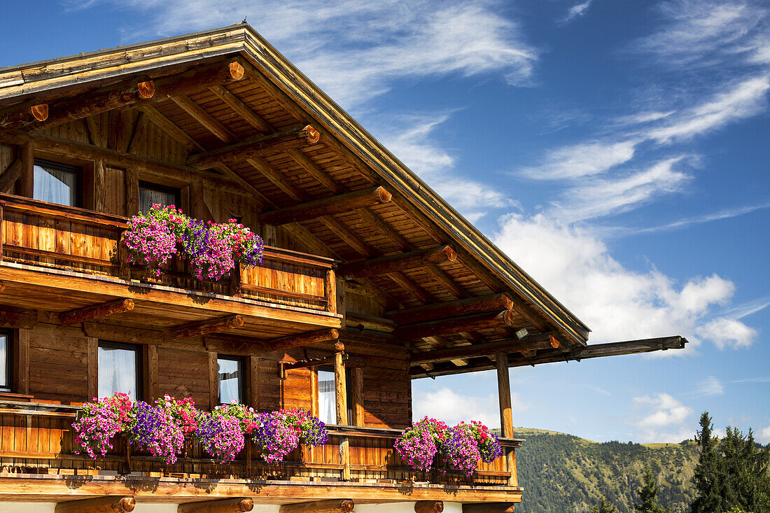 Nahaufnahme eines Holzchalets mit Blumenkästen und Balkonen mit blauem Himmel und Wolken im Hintergrund; Grainau, Bayern, Deutschland.