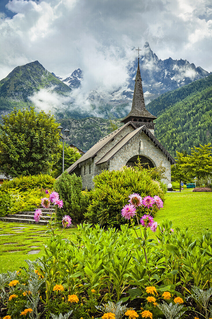 Mittelalterliche Kirche Les Praz de Chamonix und Blumengarten mit der Aiguille Dru im Hintergrund; Chamonix-Mont-Blanc, Haute-Savoie, Frankreich.