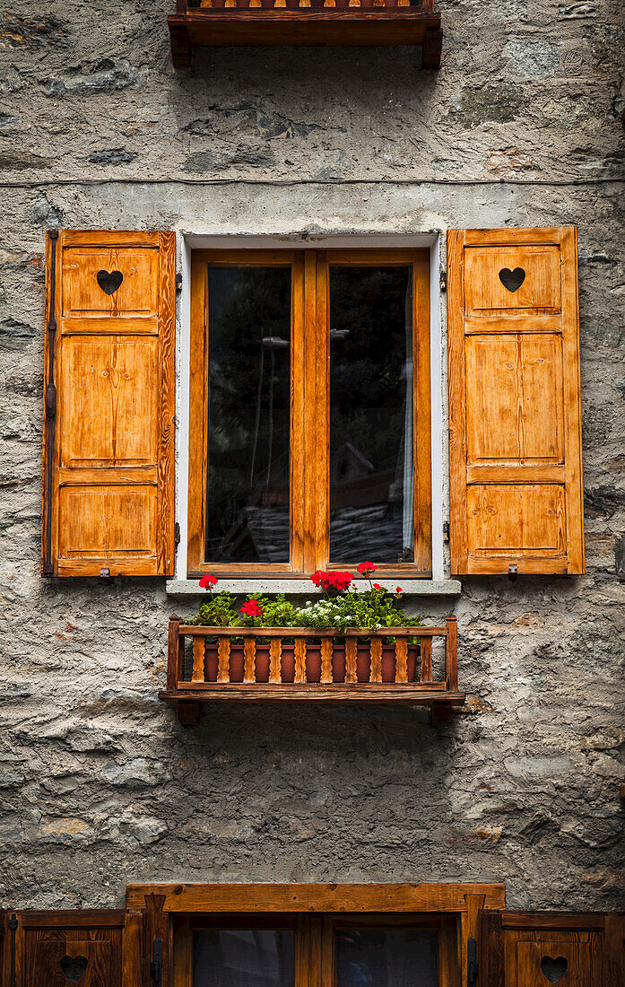 Hölzerne Fensterläden und Blumen an einem alten Steingebäude, in der Nähe von Courmayeur; Dolonne, Aostatal, Italien
