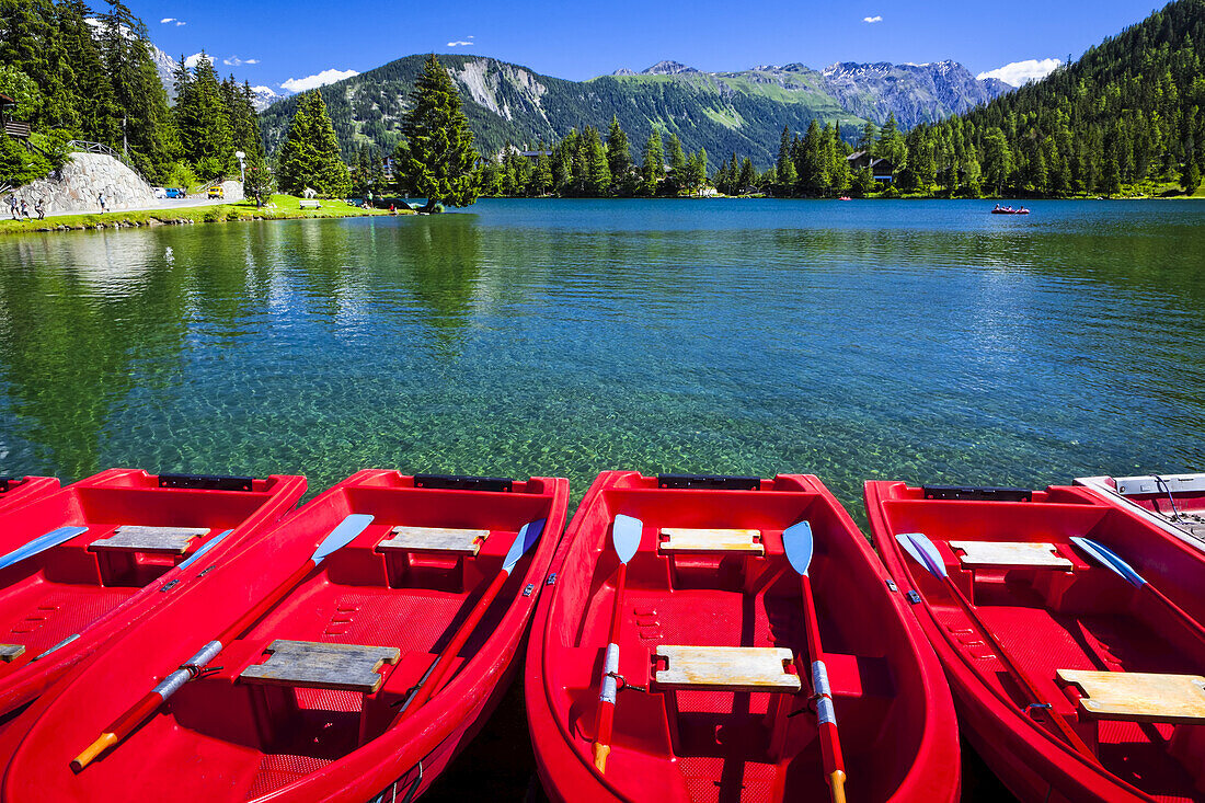 Rote Boote aufgereiht am Champex See unter blauem Himmel mit einer Bergkette im Hintergrund; Champex, Wallis, Schweiz