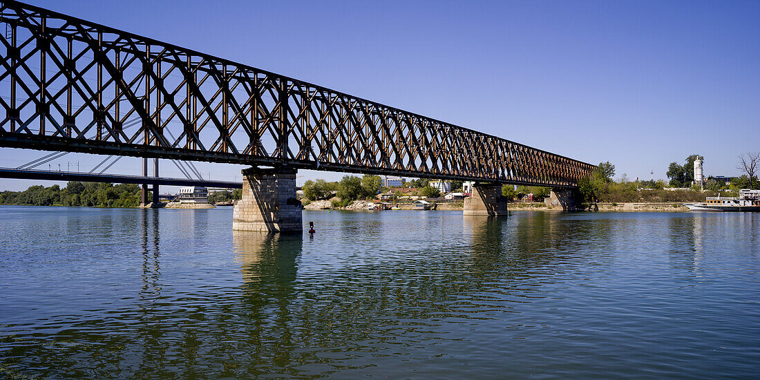 A bridge crossing the Sava River reflected in the water with blue sky; Belgrade, Vojvodina, Serbia