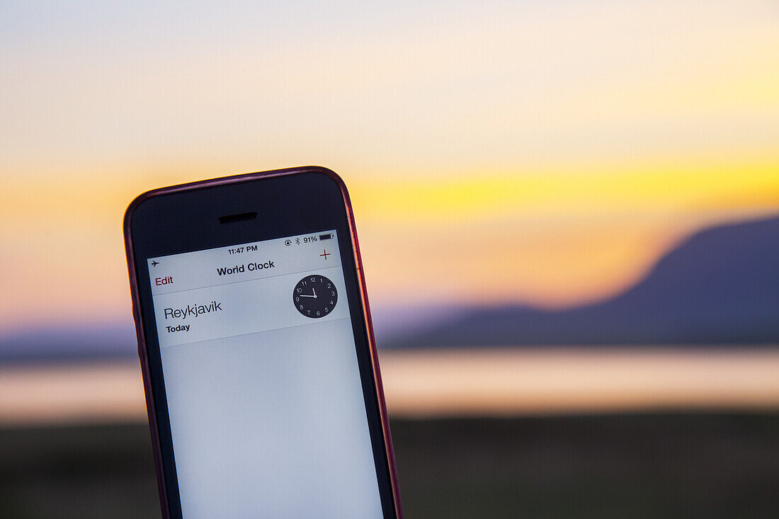 A cell phone displays the local time close to midnight in Reykjavik  close to midnight with the daylight still visible at summer solstice, when the sun doesn't fully set in Iceland even at midnight; Reykjavik, Iceland