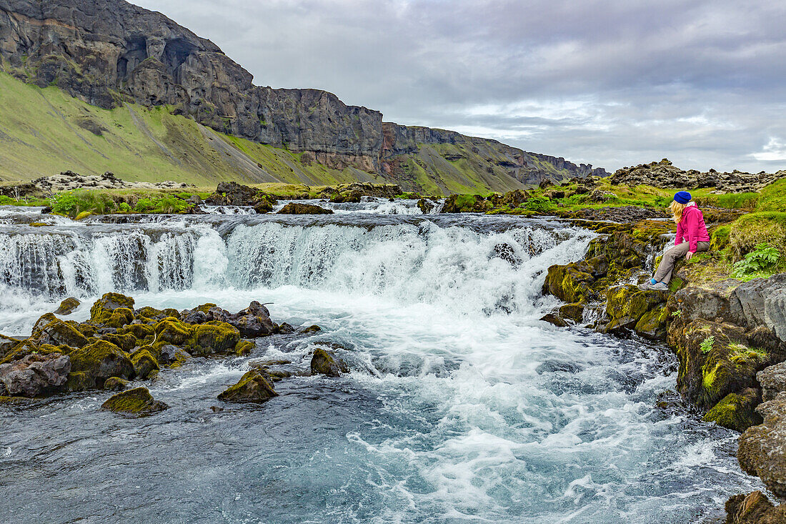 Eine Wanderin posiert für ein Foto am Rande eines Wasserfalls; Island