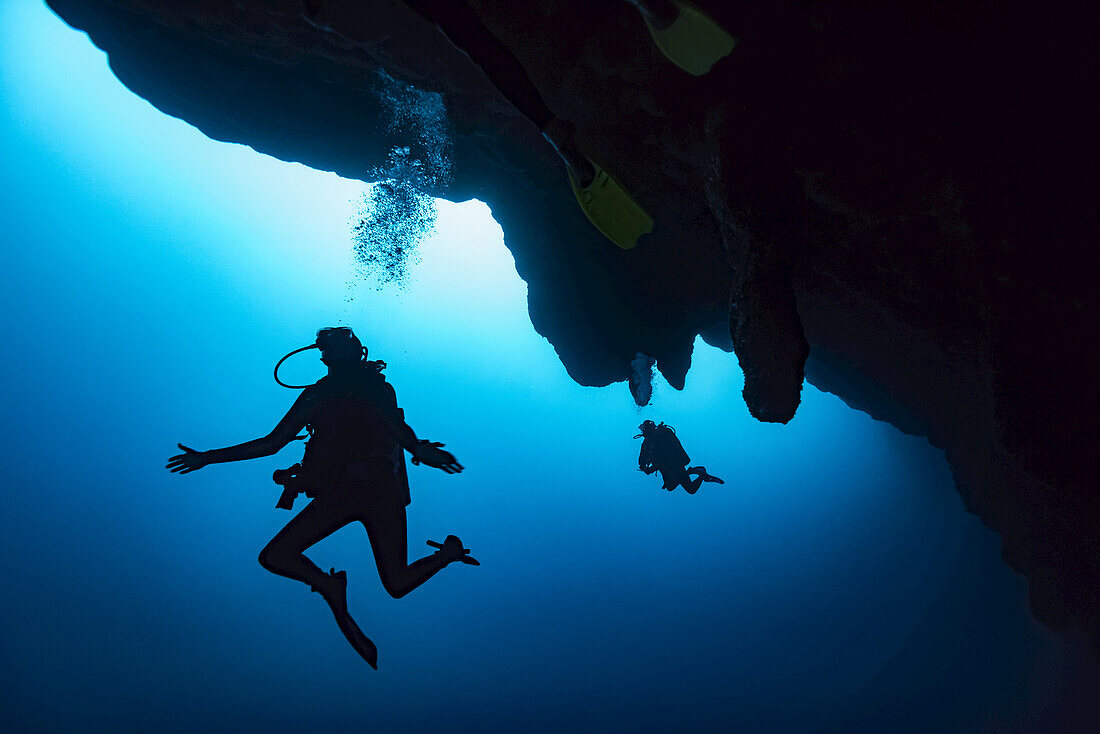 Scuba divers in the Great Blue Hole dive site on the Belize Barrier Reef. This site was made famous by Jacques Cousteau, who declared it one of the top five scuba diving sites in the world; Belize