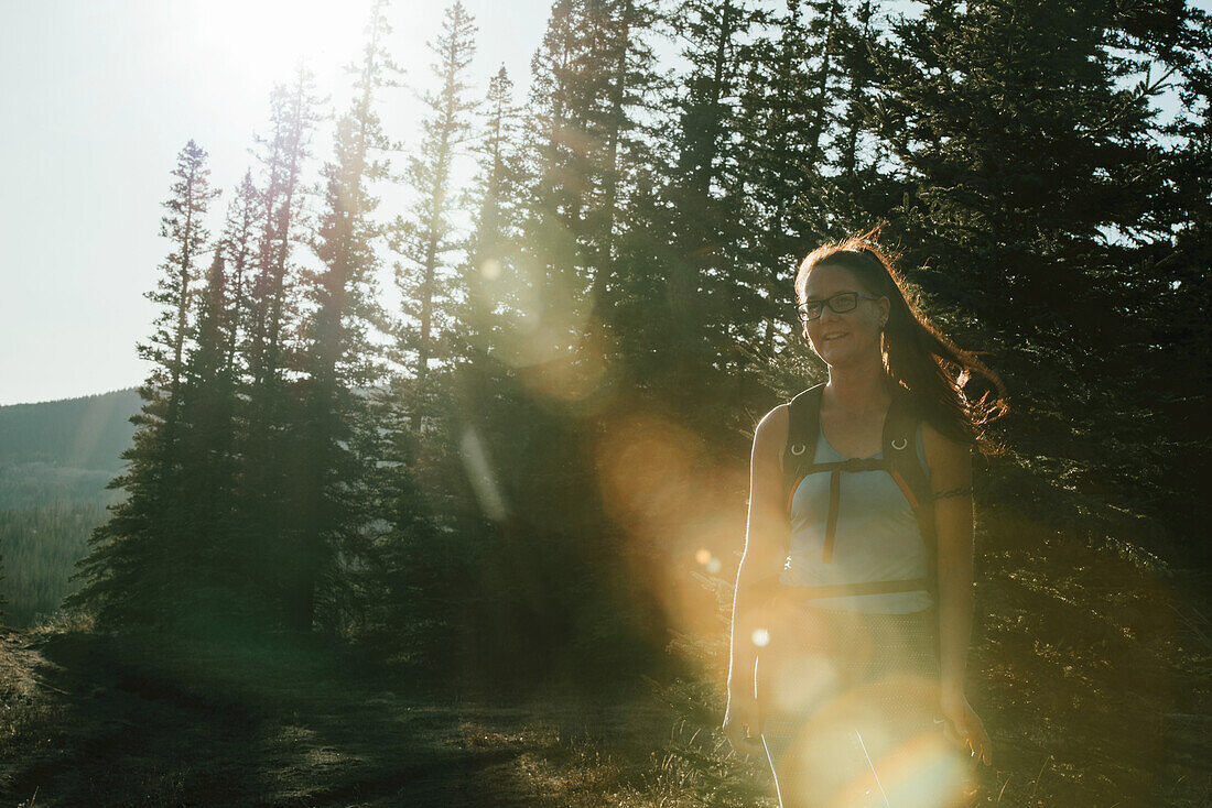 Eine Frau, die von einem Sonnenstrahl beleuchtet wird, während sie auf einem Pfad in den Rock Mountains in der Nähe von Hinton läuft; Alberta, Kanada.