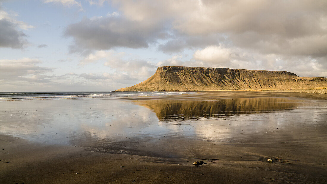 Wet black sand beach along the coast of Iceland with cliffs reflected in the water; Grundarfjorour, Iceland