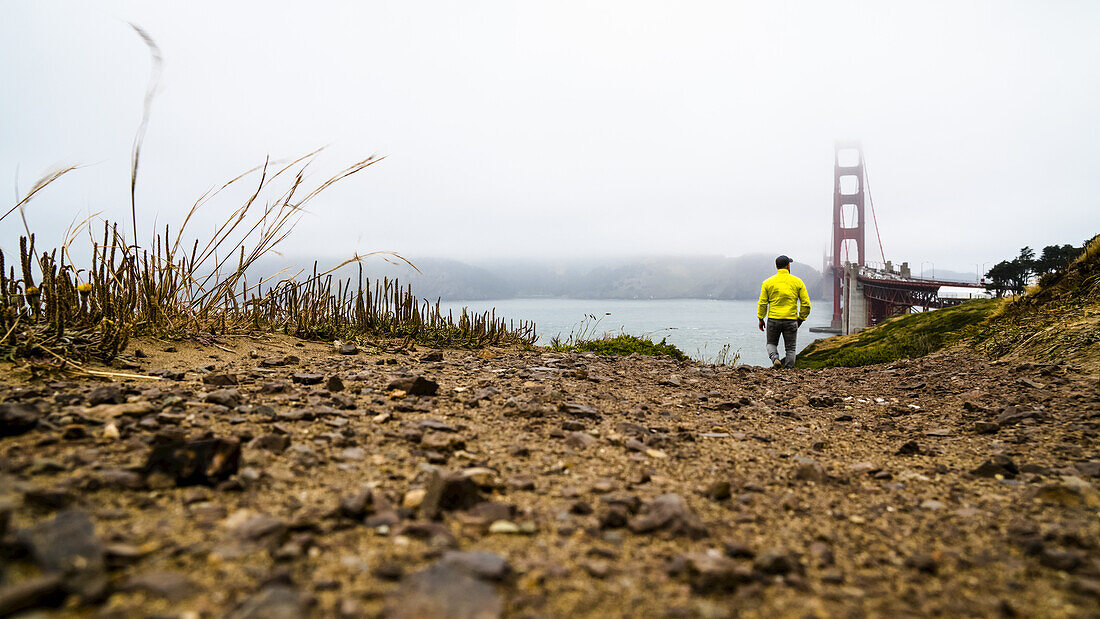 Ein Mann geht an einem nebligen Tag in der Nähe der Golden Gate Bridge spazieren; San Francisco, Kalifornien, Vereinigte Staaten von Amerika.