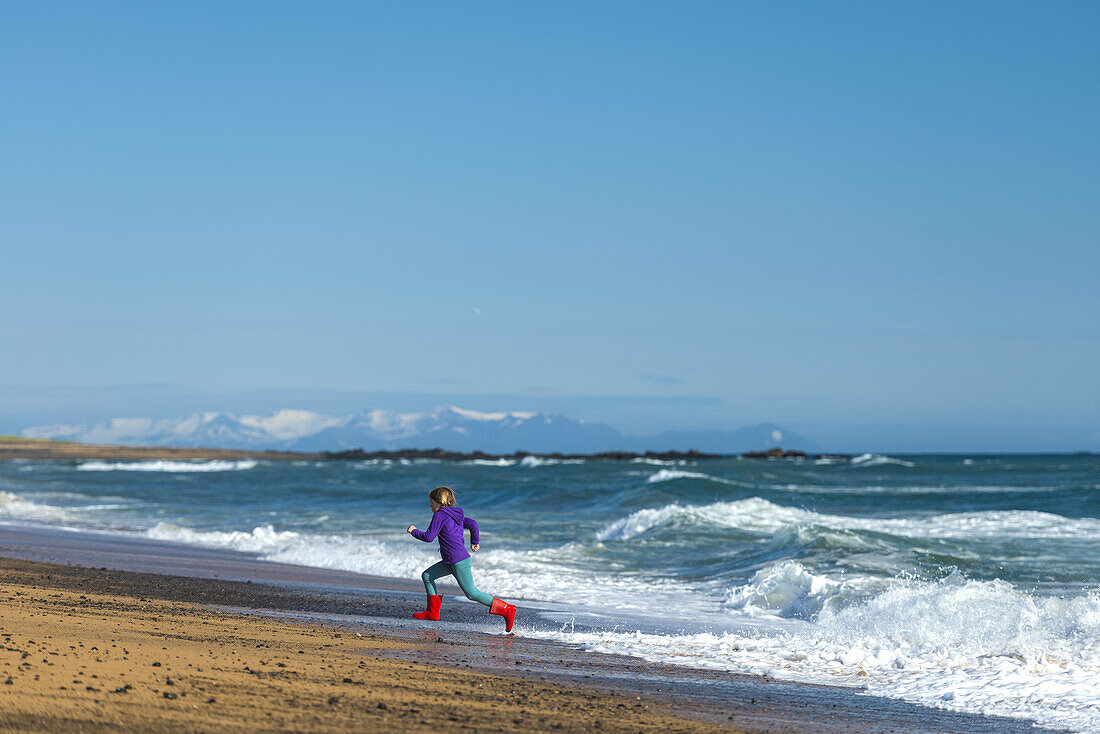 Girl running from waves on Langaholt beach; Langaholt, Iceland