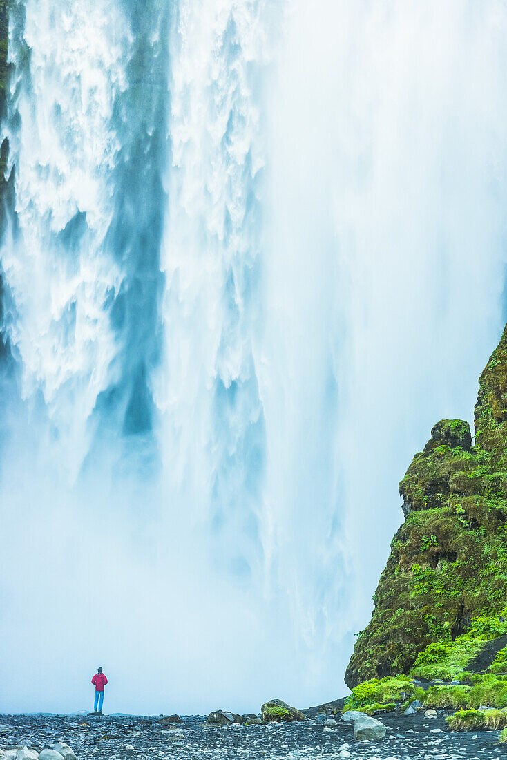Mann stehend am Fuße des Skogafoss-Wasserfalls; Island