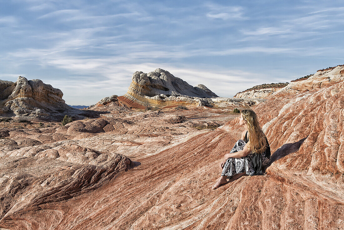 A woman sits on a rock formation enjoying the view at White Pocket, Vermilion Cliffs National Monument; Kanab, Arizona, United States of America
