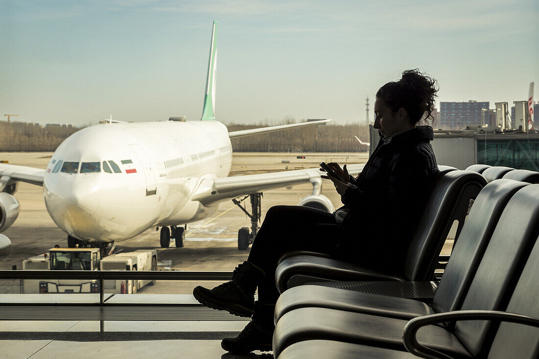 Passenger sitting in airport terminal using her smart phone, Beijing Capital International Airport; Beijing, China