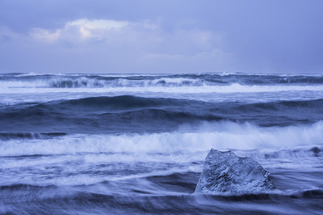 The ocean crashes around a chunk of ice on the South shore of Iceland near Jokulsarlon; Iceland
