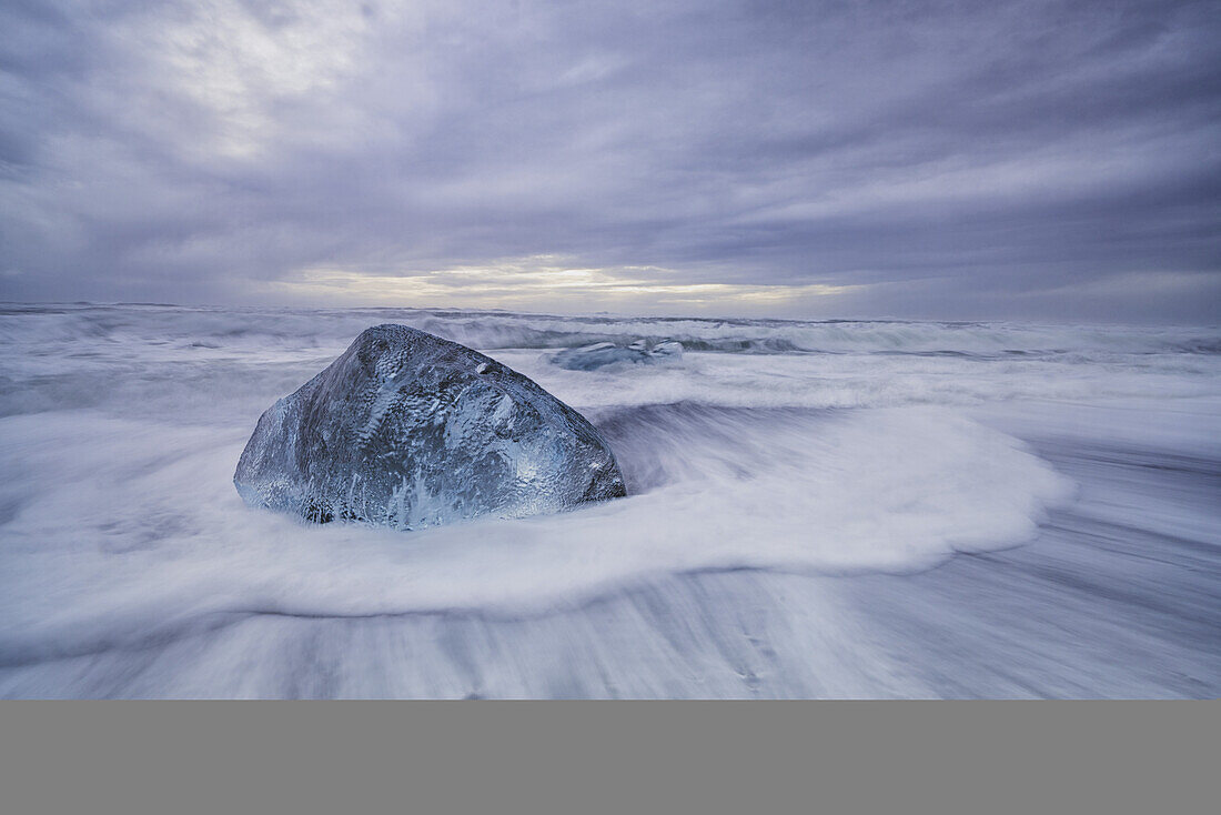 Großer Eisblock liegt an der Küste von Südisland, während Wellen an die Küste schlagen; Island