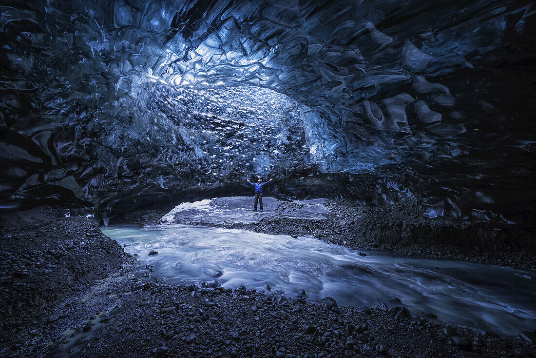 Mann, der unter einer Öffnung in der Eishöhle steht, während er unter einem Gletscher spazieren geht: Island