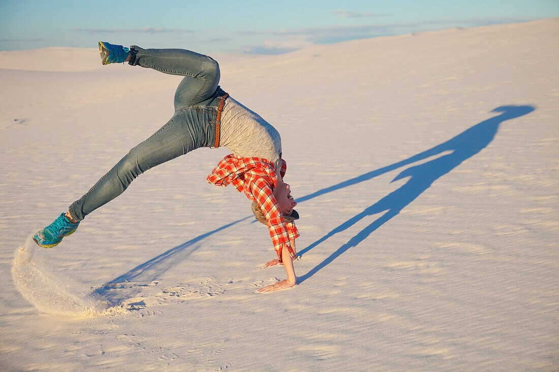Eine junge Frau vollführt eine akrobatische Bewegung auf dem weißen Sand mit blauem Himmel, White Sands National Monument; Alamogordo, New Mexico, Vereinigte Staaten von Amerika
