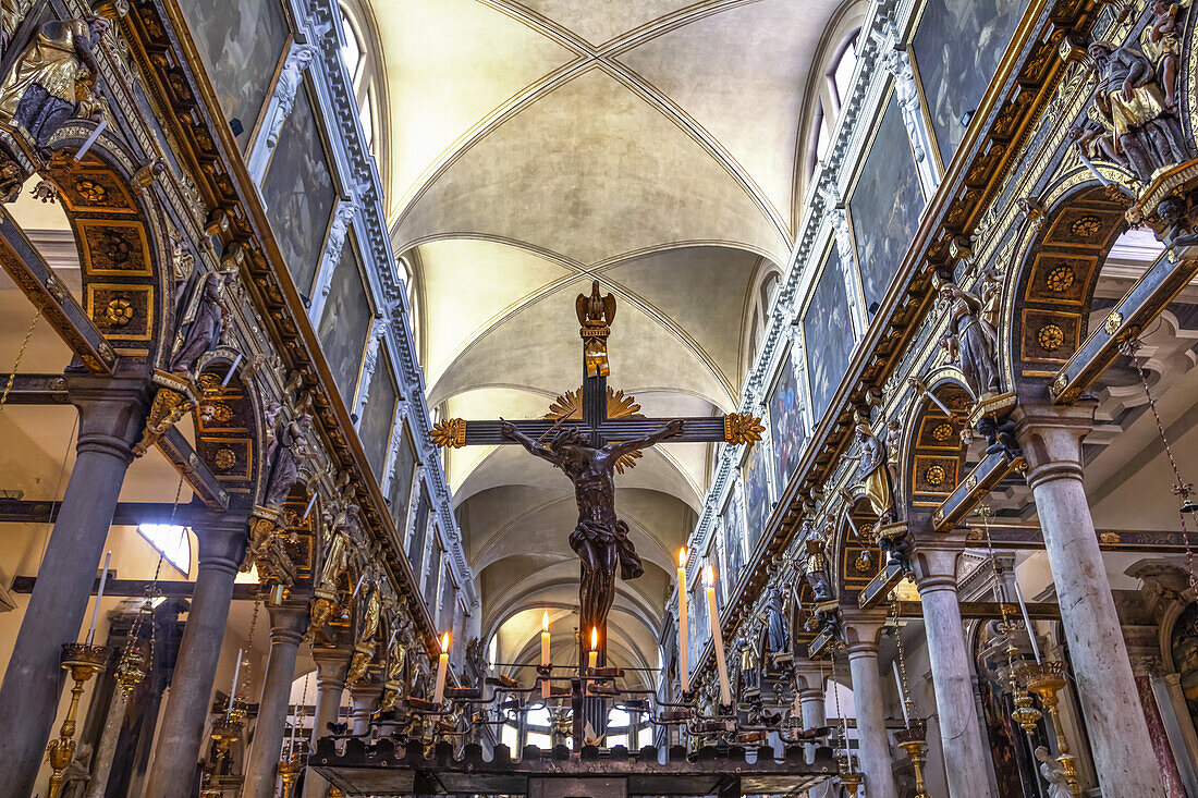 Kruzifix in einer Kirche mit verzierten, dekorativen Details an den Wänden und Bögen; Venedig, Italien.