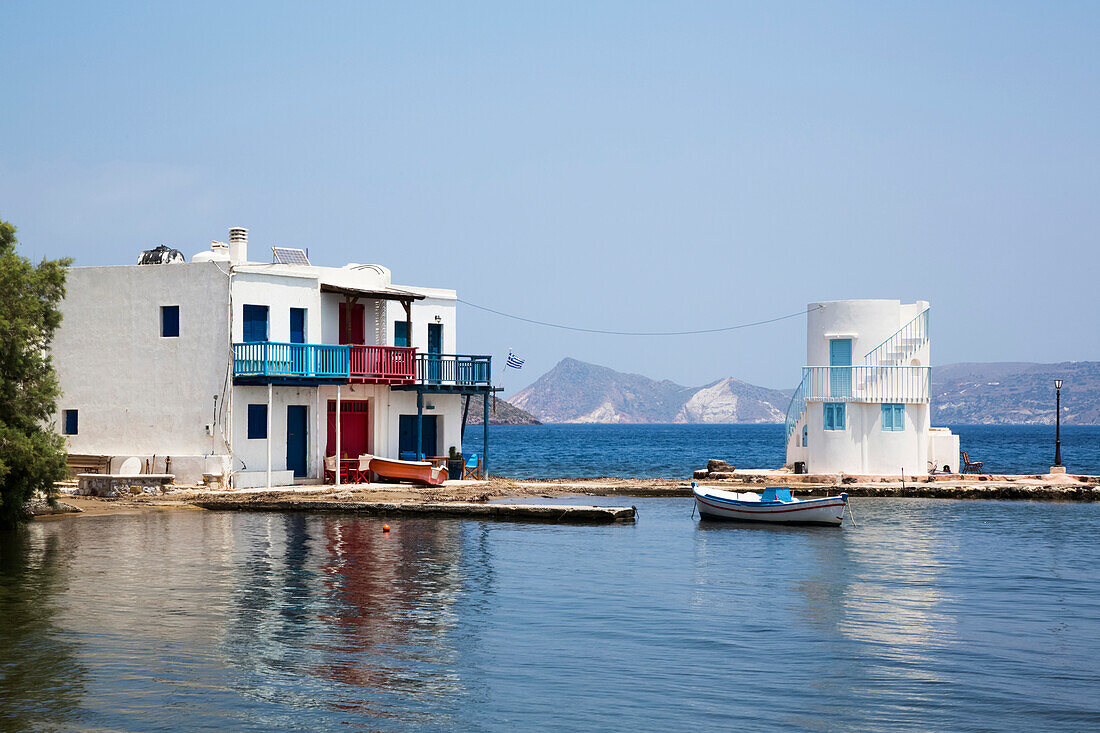 Dorf Embourios mit einem Wohnhaus am Wasser und einem kleinen Boot am Kai; Embourios, Insel Milos, Kykladen, Griechenland.