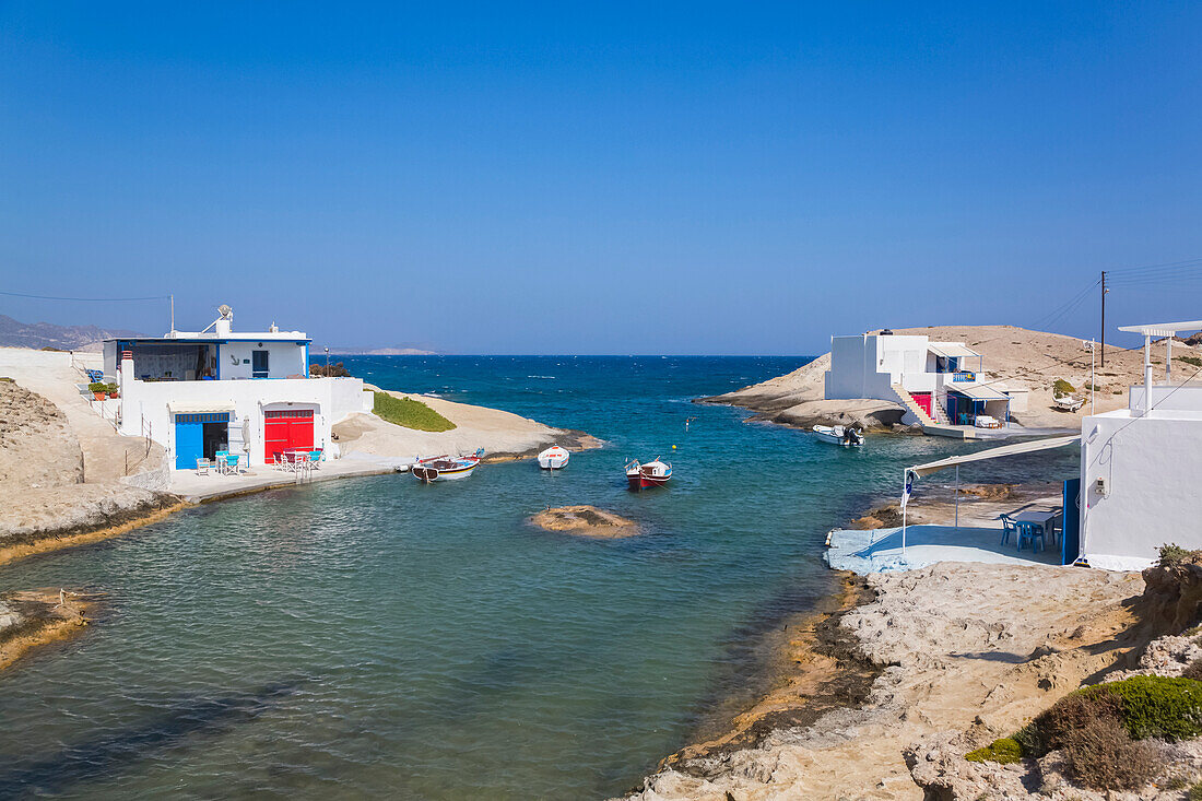 White houses with colourful accents along the shoreline with a view of the Aegean Sea and horizon with blue sky; Konstantinos, Milos Island, Cyclades, Greece