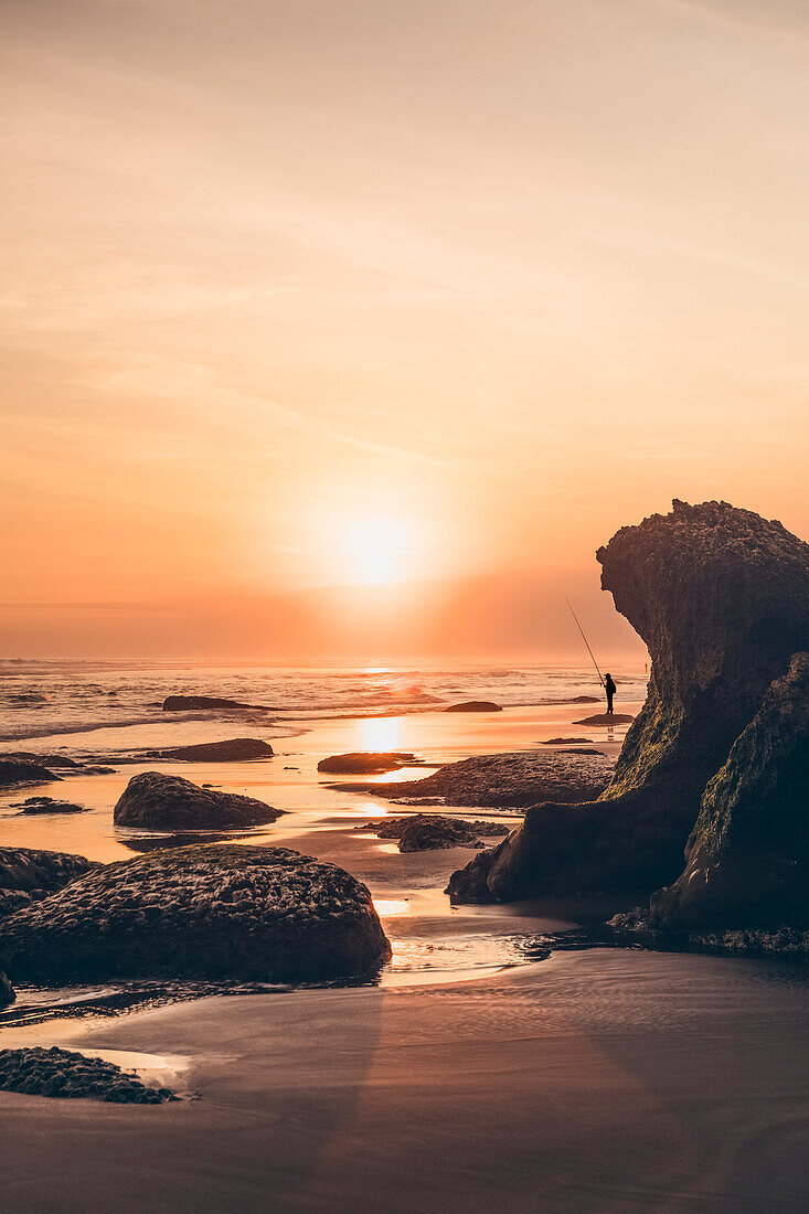 Sonnenuntergang am Parangendog Strand mit einer Person, die vom Strand aus fischt; Purwosari, Yogyakarta, Indonesien