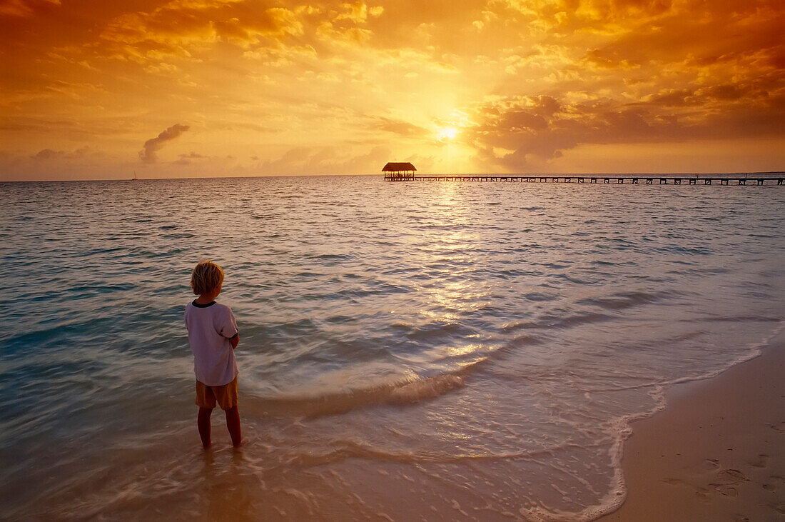 Junge am Strand bei Sonnenaufgang