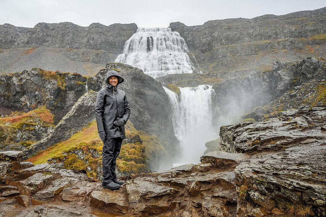 Touristinnen stehen auf einem Felsen bei Dynjandi (auch als Fjallfoss bekannt), einer Reihe von Wasserfällen in den Westfjorden, Island. Die Wasserfälle haben eine Gesamthöhe von 100 Metern; Isafjardarbaer, Westfjorde, Island