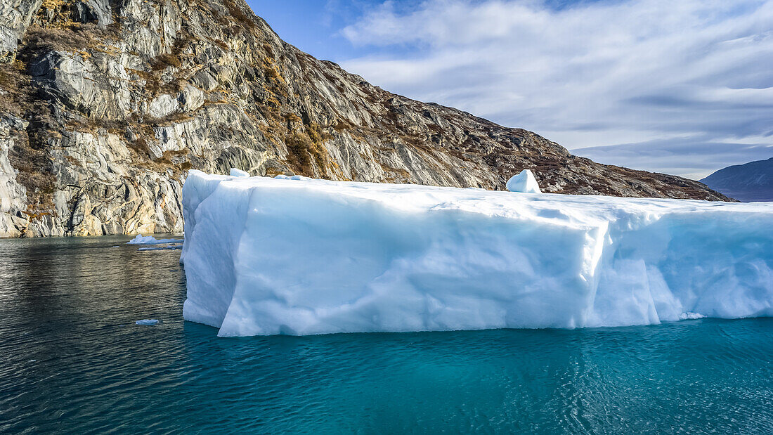 Eisberg in blauem Wasser vor der zerklüfteten Küste Grönlands; Sermersooq, Grönland