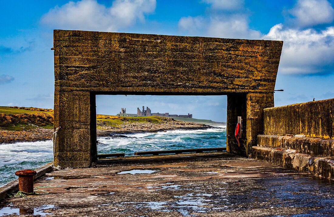 Blick auf Dunstanburgh Castle von einem Pier mit Zementstruktur am Hafen von Craster; Craster, Northumberland, England.