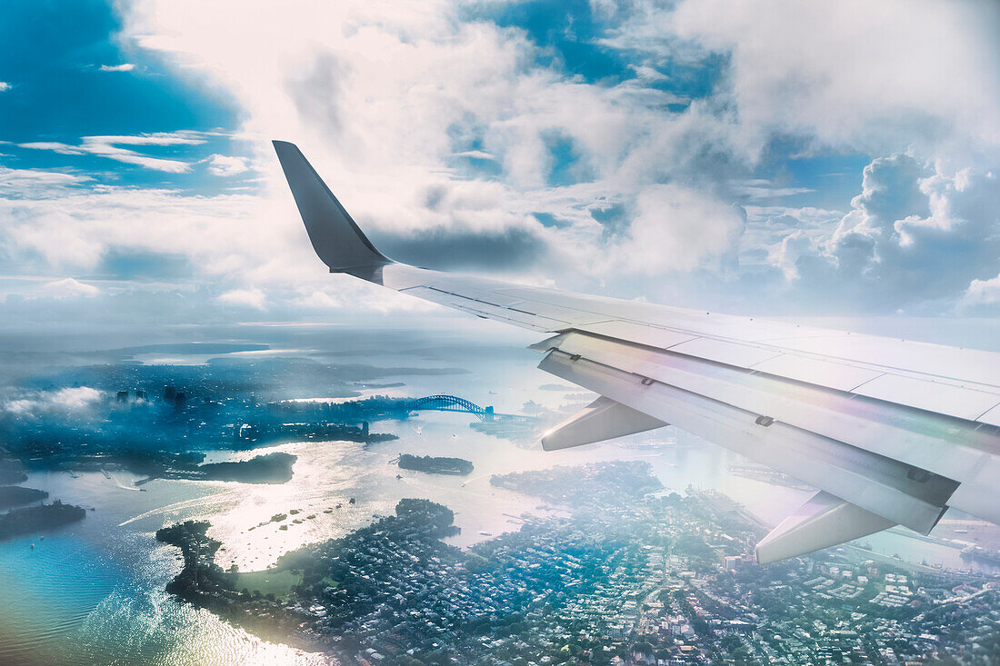 Close-up of plane's wing from an airplane, flying over the coast of downtown Sydney on a sunny day; New South Wales, Australia