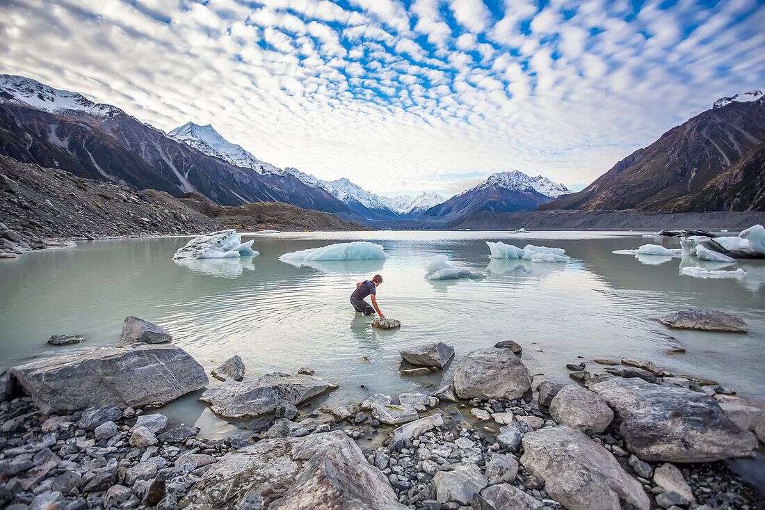 Man cautiously walking out into the water of the icy glacial lakes of Mount Cook National Park; Canterbury, New Zealand