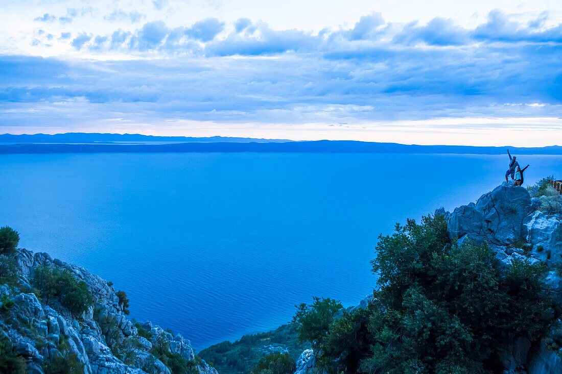 Die atemberaubenden, hoch gelegenen Klippenstraßen entlang der kroatischen Küste. Diese Straße ist der Sveti Jure Bergpass, der durch das Biokovo-Gebirge führt. Reisende halten für ein Sonnenuntergangsfoto an; Podgora, Gespanschaft Split-Dalmatien (Splitsko-dalmatinska zupanija), Kroatien