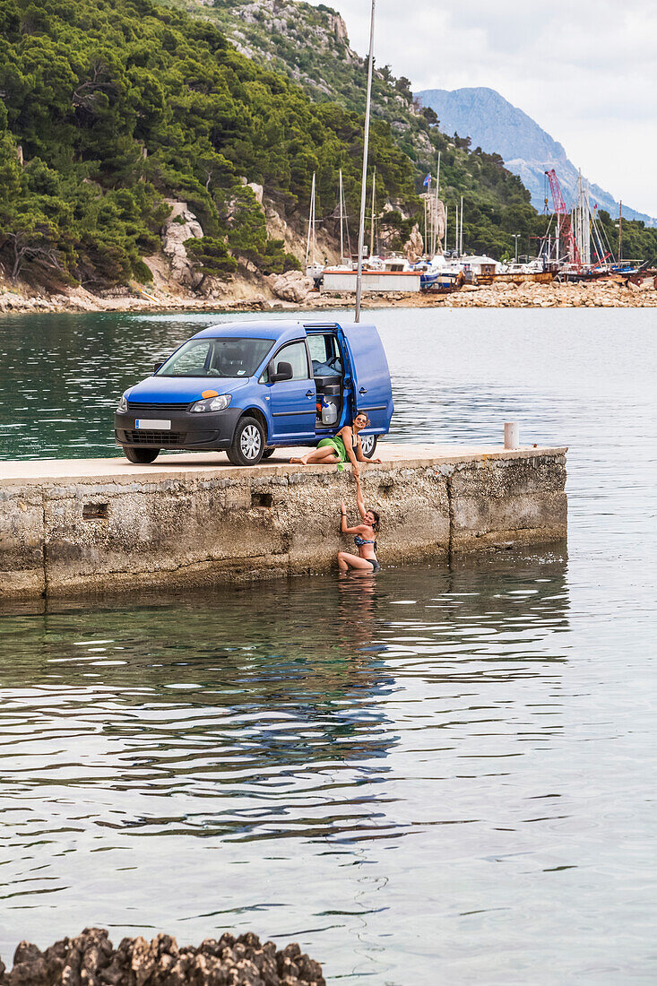 Reisende Frauen halten für ein frühmorgendliches Bad im Meer an, nachdem sie auf einem Road Trip in ihrem Van gezeltet haben; Podgora, Gespanschaft Split-Dalmatien (Splitsko-dalmatinska zupanija), Kroatien