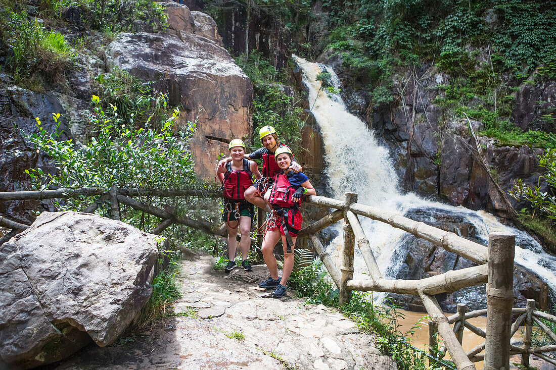 Portrait of friends standing by a log fence next to the Datanla Falls, ready for canyoning; Da Lat, Vietnam. Canyoning is one of the most popular activities in Dalat. The Datanla Falls and the rivers running from it are great for abseil, cliff jumping, rock slides, and floating downriver.