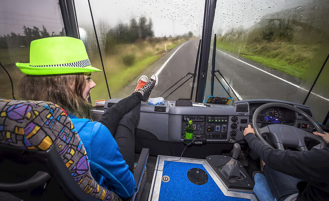 A girl sits in the front seat of a bus as they travel through New Zealand, Tongariro National Park; Manawatu-Wanganui, New Zealand