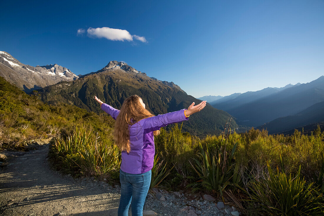 Woman hiker raises her arms in awe of the surrounding beauty of nature on the Key Summit Track, part of the Routeburn Track; Fiordland National Park, Southland, New Zealand