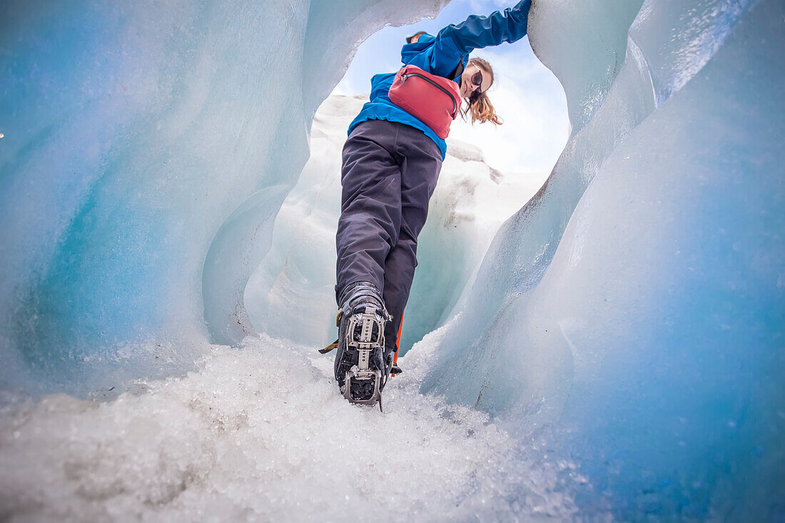 Woman Hiker wearing spiked traction cleats while walking on ice through the famous Franz Josef Glacier; West Coast, New Zealand